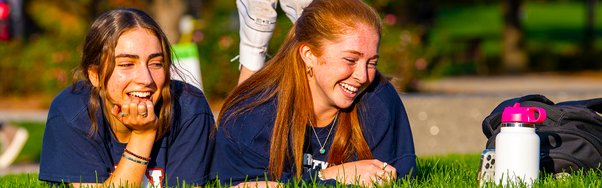 students laying in the grass, laughing at a smartphone screen students laying in the grass, laughing at a smartphone screen